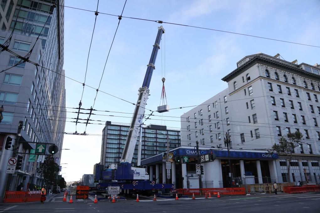 A crane moves substation equipment into an access area cut into Market St. in San Francisco.