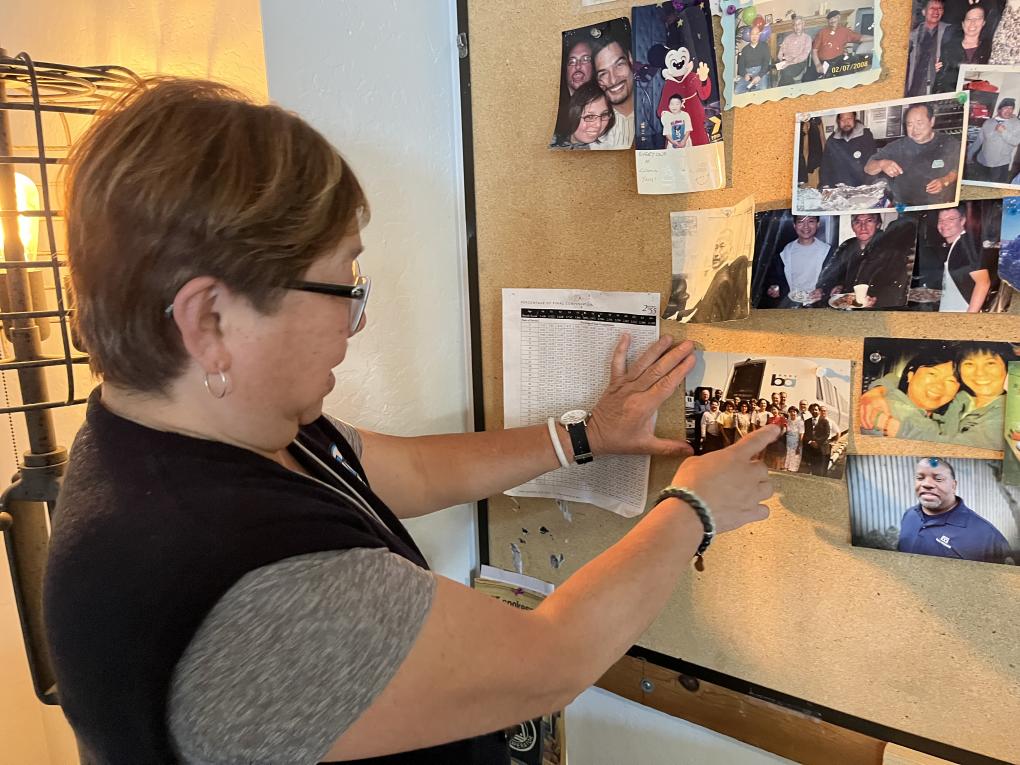 Mama Linda points to a photo of her Train Operator graduating, July 1991, on the massive corkboard at Daly City Yard. 