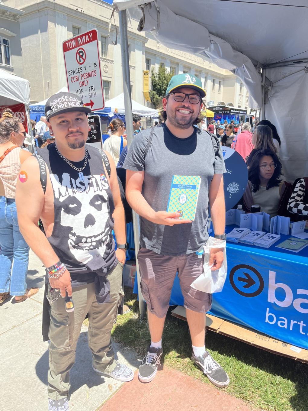 Two people in front of the booth with a BART Lines chapbook