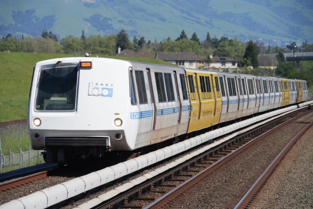 A legacy BART train on the track with green hills behind it