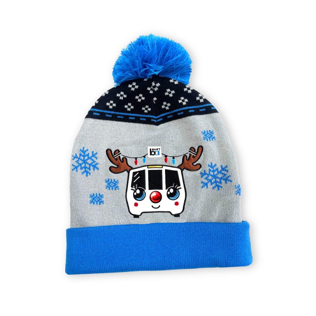 BART holiday beanie with a blue pom pom and rim and a smiling BART train with antlers and a red nose. Snowflakes float around it.