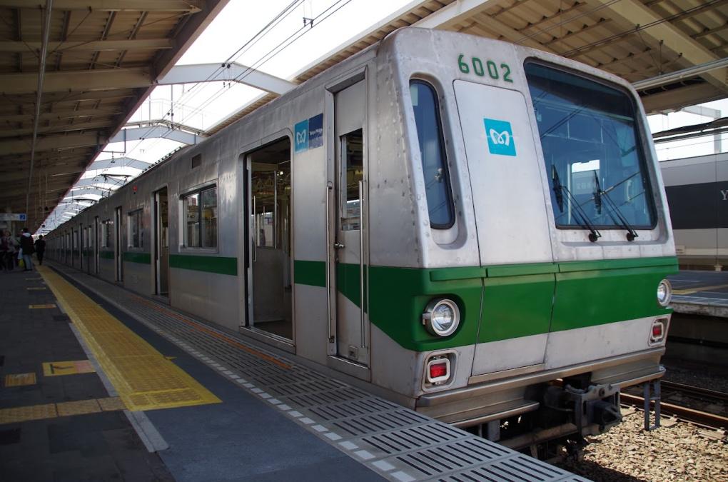 A train parked at a platform in Tokyo, displaying its distinctive teal and green livery and logo.