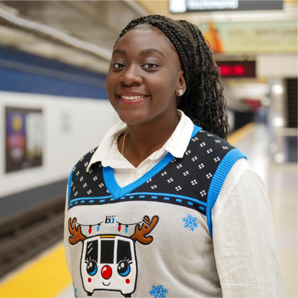 Person smiling in a BART holiday vest in front of a BART train 