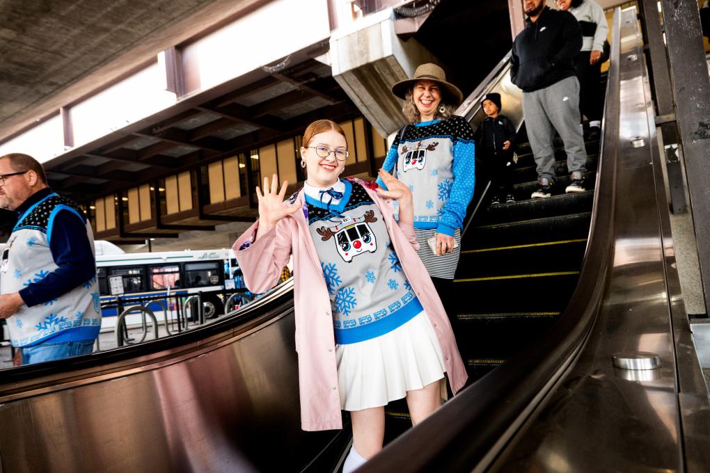 Two people in BART sweaters riding down the escalator. 